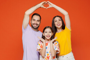 Young parents mom dad with child kid daughter teen girl in basic t-shirts hold hands above head showing shape heart with hands heart-shape sign isolated on yellow background studio Family day concept - obrazy, fototapety, plakaty