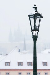 Fototapeta na wymiar Street lamp in snowy Prague. In the background snow-covered houses and Prague Castle. Christmas atmosphere.