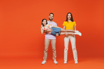 Fototapeta na wymiar Full body young smiling cheerful happy parents mom dad with child kid daughter teen girl in basic t-shirts hold carrying baby isolated on yellow background. Family day parenthood childhood concept