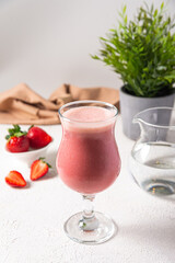 strawberry protein shake in glass. raw strawberries blended with protein powder and water served in glass. raw berries, clean water, white kitchen background.