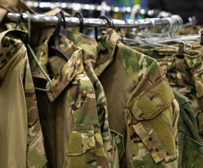 Department in the men's military clothing store. Camouflage uniforms hang on hangers in a military store