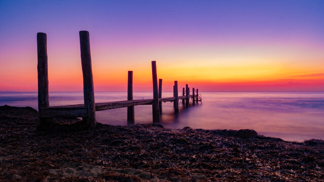 Un ponton en bois se dessine en ombre chinoise durant lever de soleil d' une plage de Ramatuelle dans le Golfe de Saint-Tropez