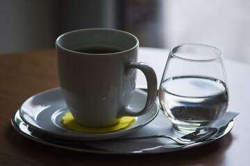 A cup of matcha tea with a glass of water, complete with a spoon. Everything on a pad and wooden table.