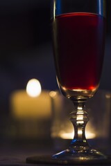 A glass of red wine on a table. In the background burning candles.