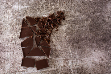 a broken bar of dark chocolate on a concrete background.