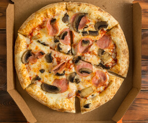 freshly baked pizza with mushrooms and ham in a cardboard box on a wooden table