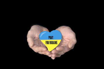Text Pray for Ukraine. Male hands on a black background, showing hand Flag of Ukrainian in heart shape. Power of hope or love and devotion. hands with faith in religion and belief in God. Conflict