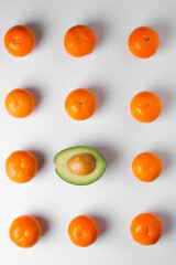 eleven oranges and one avocado on a gray background