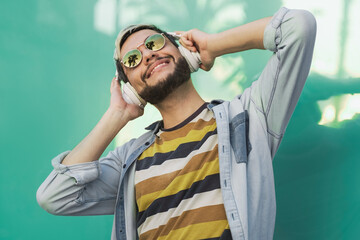 Young hipster man dancing and listening music on mobile phone wearing headphones outdoor - Focus on face