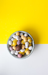 Easter colorful flat lay. Easter chocolate eggs of vibrant colors on bright yellow and white background.  Culture food and easter celebration.