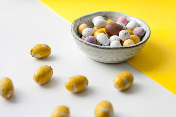 Easter colorful flat lay. Easter chocolate eggs of vibrant colors on bright yellow and white background.  Culture food and easter celebration.