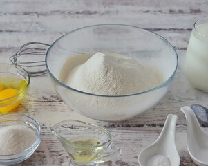 On a white wooden table are the ingredients for baking a dessert dish - flour, eggs, vegetable oil, sugar, salt, soda, milk or kefir. Photo for baking recipe.