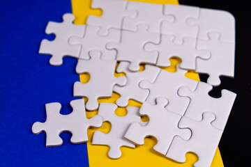 Fototapeta premium Missing jigsaw puzzle pieces. Business concept. Fragment of a folded white jigsaw puzzle and a pile of uncombed puzzle elements against the background of a colored surface.