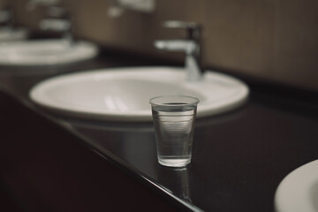 a transparent plastic glass with clean water on a black table near the washbasin and water tap in the changing room of the gym