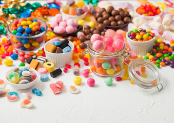 Pink lollipop candies in jar with various milk chocolate and jelly gums candies on white background with liquorice allsorts and strawberry bonbons