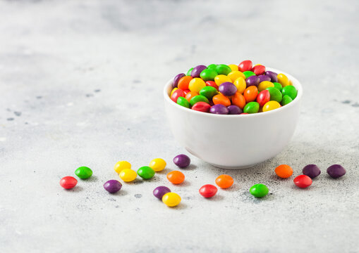 Multicolored mix of fruit candies in white bowl on light background.