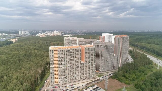 Aerial drone shot of apartment buildings next to the highway on cloudy day. Aerial shot over community apartment complex with parking and cars surrounded by forest. Gloomy cloudy sky. Lots of cars dri