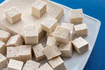 Tofu cut in cubes. Firm tofu on white plate. Vegan protein food.