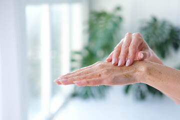 Close-up woman is hands with coffee massage scrub on monstera blurred background. Cosmetology, hand...