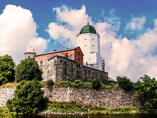 Fototapeta premium Castle with loopholes and masonry in the ancient city against a bright blue sky with clouds, among trees, view, exterior