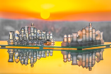 A glass chess set on a glass  table seen from the side with a horizontal mirror reflection. Blurred...