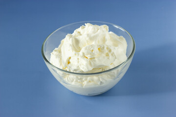Homemade, glass bowl of whipped egg whites cream on blue kitchen table background, top view, closed up. Horizontal plane.