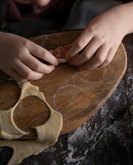 Kid making pelmeni (meet dumplings) of dough on wooden table with ingredients flour, oil, salt,...