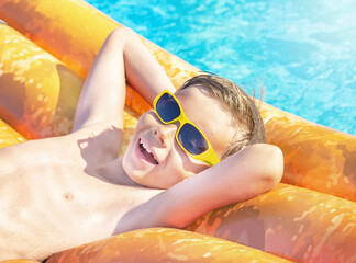 Happy nine years old child (boy) in yellow sunglasses having fun on orange inflatable ring (air...