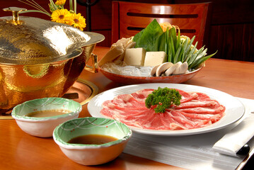 Shabu-shabu dish with vegetables, noodles, sauces, tofu and fondue burner on wooden table
