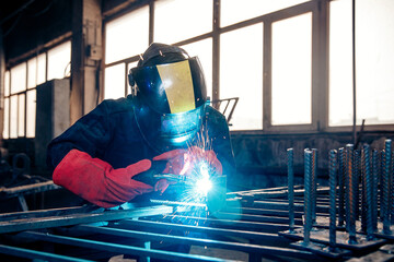 Welder in protective uniform with mask. Factory industrial worker on workplace with spark