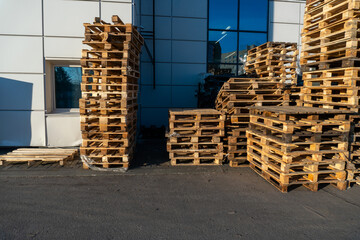 A stack of wooden pallets in an internal warehouse. An outdoor pallet storage area under the roof next to the store. Piles of Euro-type cargo pallets at a waste recycling facility.