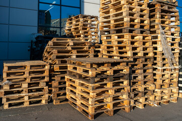 A stack of wooden pallets in an internal warehouse. An outdoor pallet storage area under the roof next to the store. Piles of Euro-type cargo pallets at a waste recycling facility.