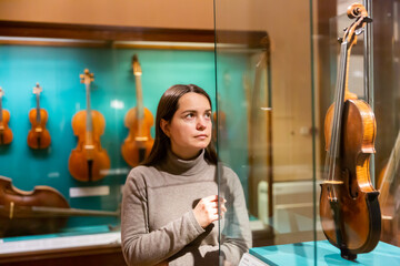 Portrait of interested adult brunette visiting exhibition of medieval musical instruments in historical museum .. - obrazy, fototapety, plakaty