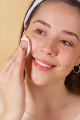 portrait young woman uses creams of her face. Isolated on a beige background. Happy healthy model skin care routine