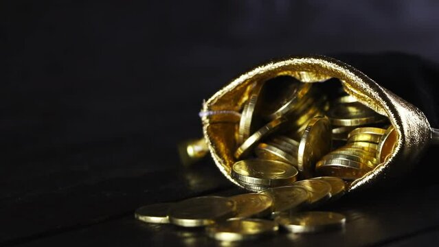 A bag with gold coins on a wooden background. The money in a black bag on a wooden table. Treasure Hunt. A Purse with money. Wallet wit gold coins.