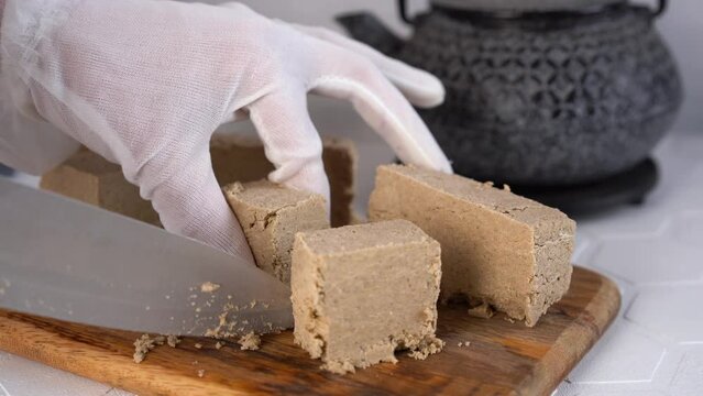 The chef cuts traditional eastern dessert halva into slices with knife. Close-up