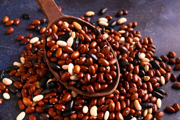 Red, black, white beans in a wooden spoon on a rustic table.