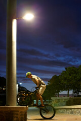 Never sleep - just ride. Shot of a man doing tricks on his bike at night under a street light.