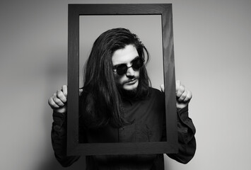 Black and white portrait of attractive man with long hair, holding a dark frame.