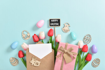 A bouquet of tulips with a postcard, a gift and wooden Easter eggs with a plaque on a light blue background.