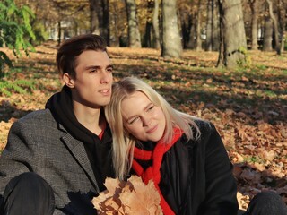 A young couple are sitting in a park or forest. A couple in love - a blonde girl and a blonde guy. The guy and the girl look into the distance in one direction and dream. Joint walk. Valentine's Day.