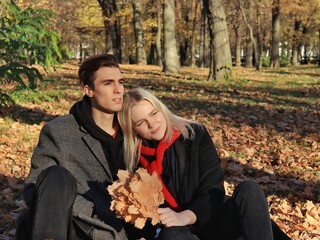 A young couple are sitting in a park or forest. A couple in love - a blonde girl and a blonde guy. The guy and the girl look into the distance in one direction and dream. Joint walk. Valentine's Day.