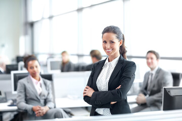 Positive about her career in the company. Pretty young businesswoman standing confidently in the office with her coworkers behind her - portrait.