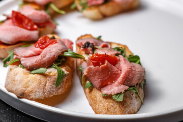 Sandwiches with tomatoes, chopped meat and fresh herbs on a large plate.