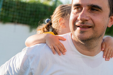 Side view of smiling father carrying cheerful girl on back while spending time together at football...