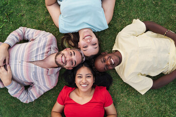 Happy multicultural friends from Africa, Latin America and Europe smiling and looking to camera in circle lying on the grass