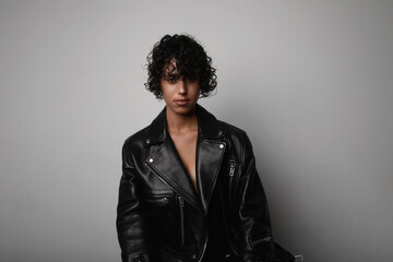 Obraz premium Young confident woman wears biker jacket looking at the camera on white wall.