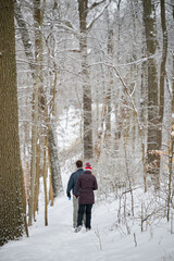 Fototapeta na wymiar PITTSBURGH, PA, USA - FEBRUARY 5TH 2022: A middle-aged father is hiking with his teenage daughter and their dog in the frozen winter forest covered in snow after an ice rain hit Pennsylvania.