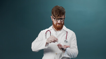 A man in a white medical gown cleans his hands with alcohol