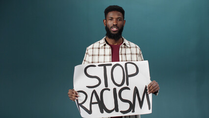 An attractive black man stands and shows a poster against racism